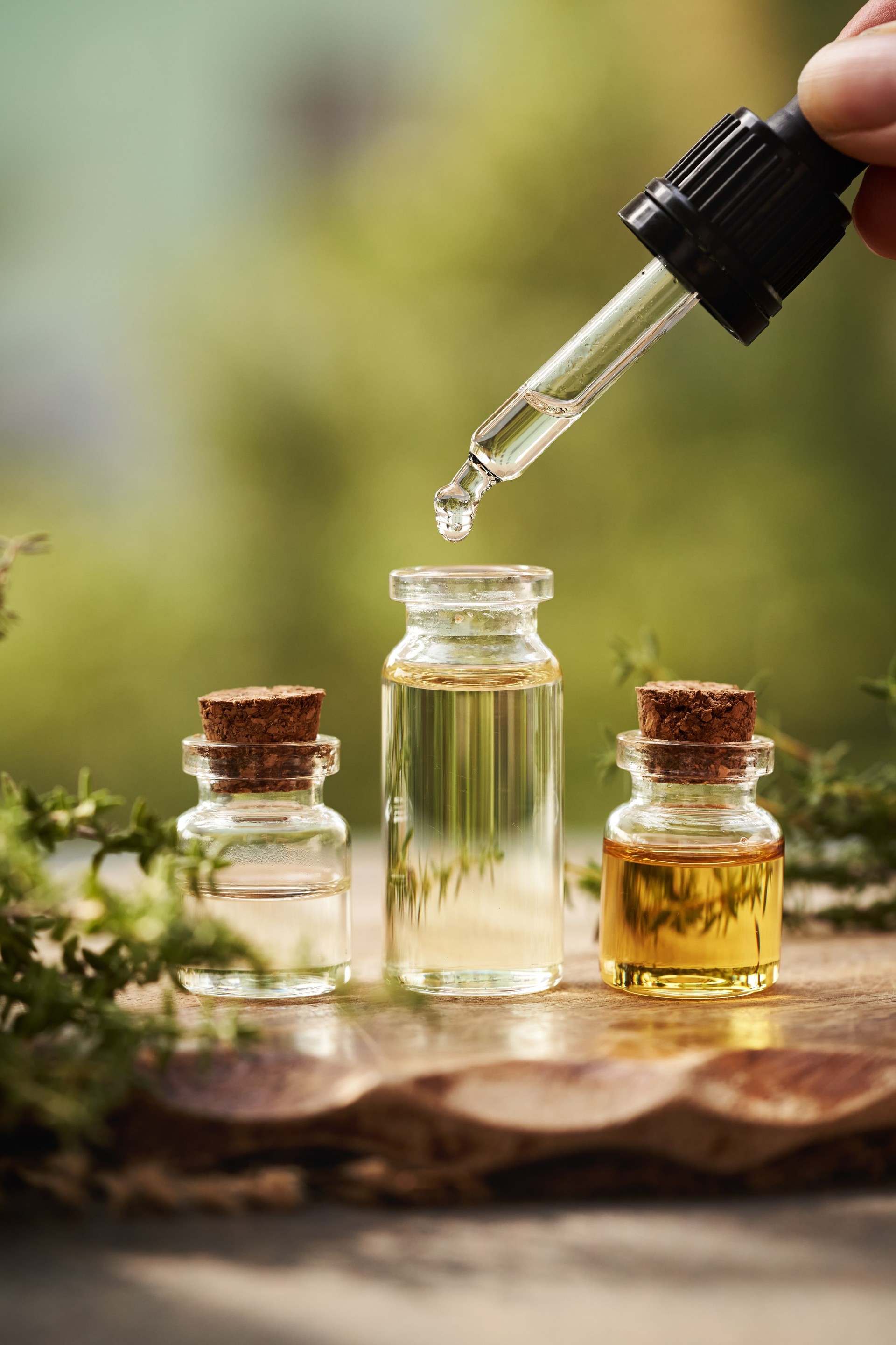 Drop of aromatherapy essential oil falling from a pipette into a bottle outdoors in nature